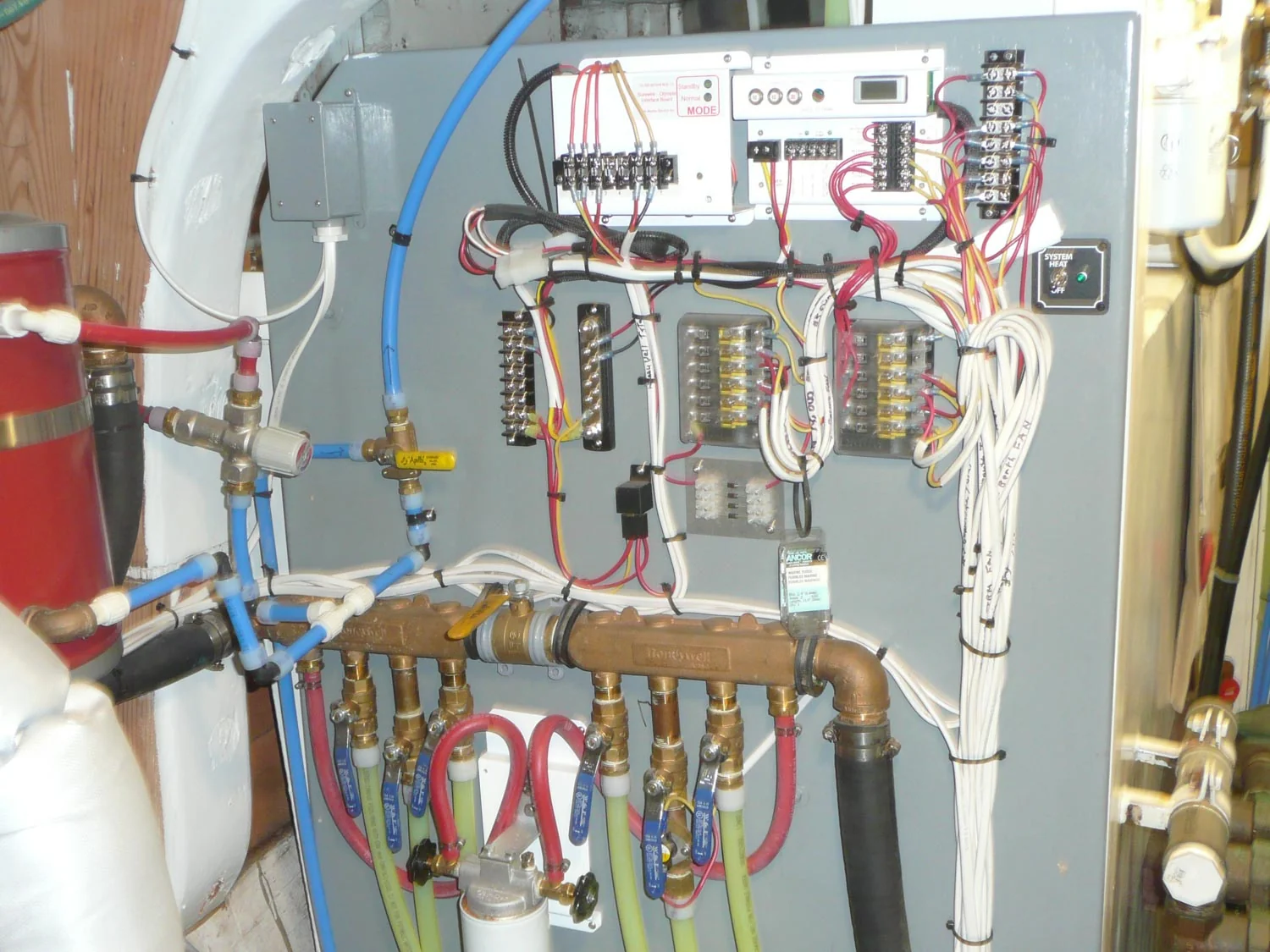 Electrical installation with terminal blocks, fuse banks and wiring above a plumbing manifold.