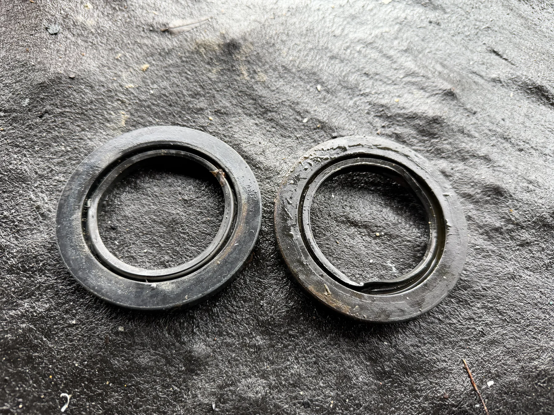 Two removed circular stabilizer shaft seals lying on a dark surface.