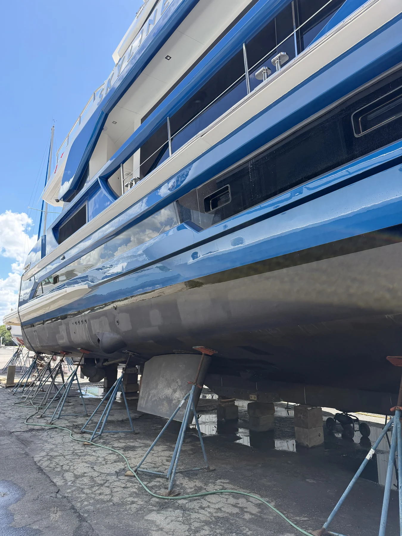 Large blue and white motor yacht supported on stands in a boatyard.