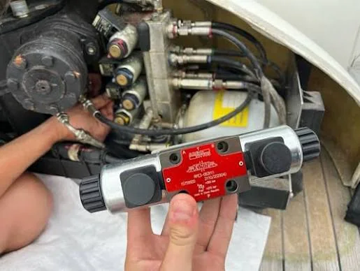 Removed marine hydraulic control valve held in front of a connected pump and manifold assembly