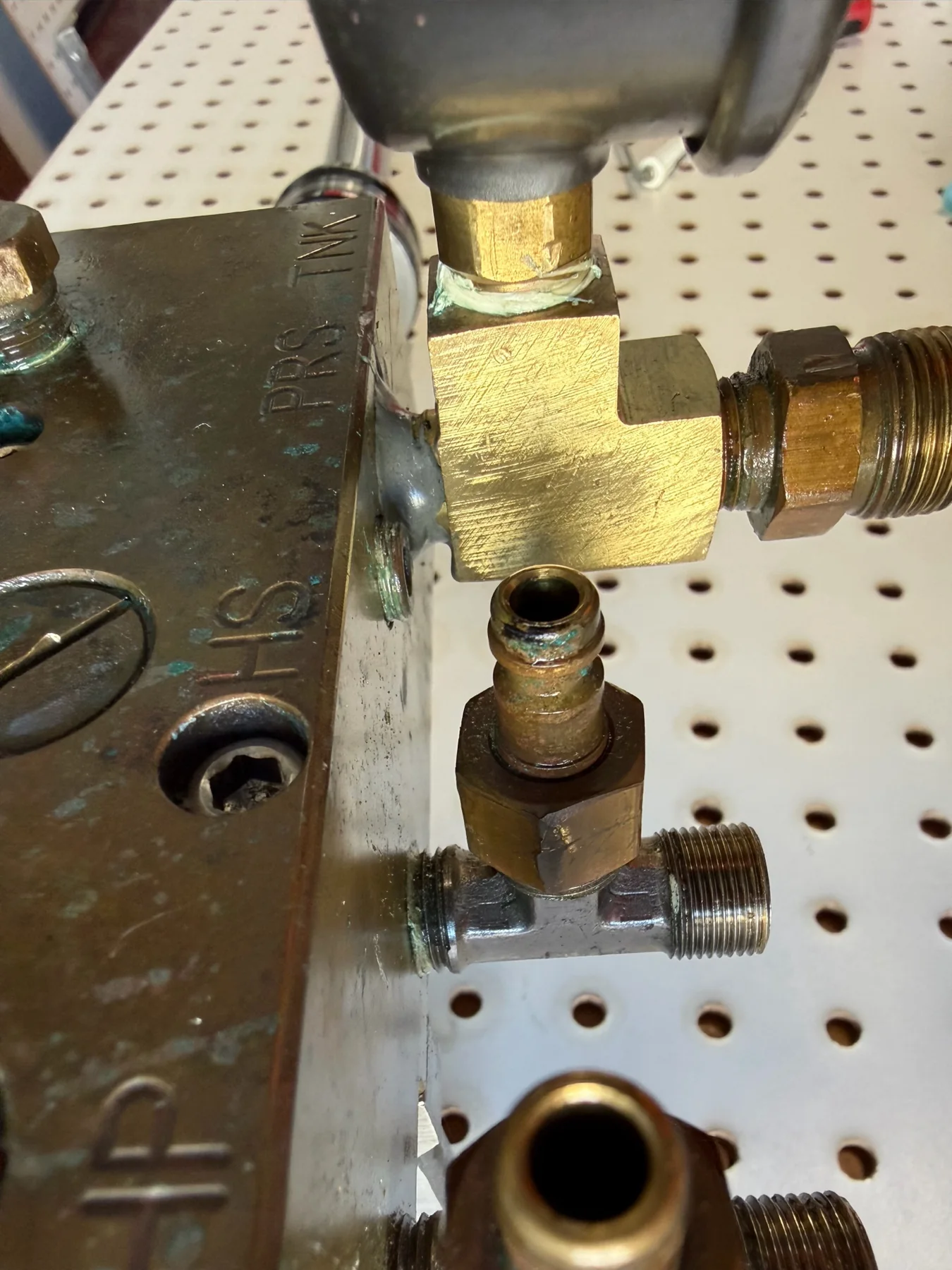 Hydraulic manifold block with brass fittings and pressure gauge on a workbench