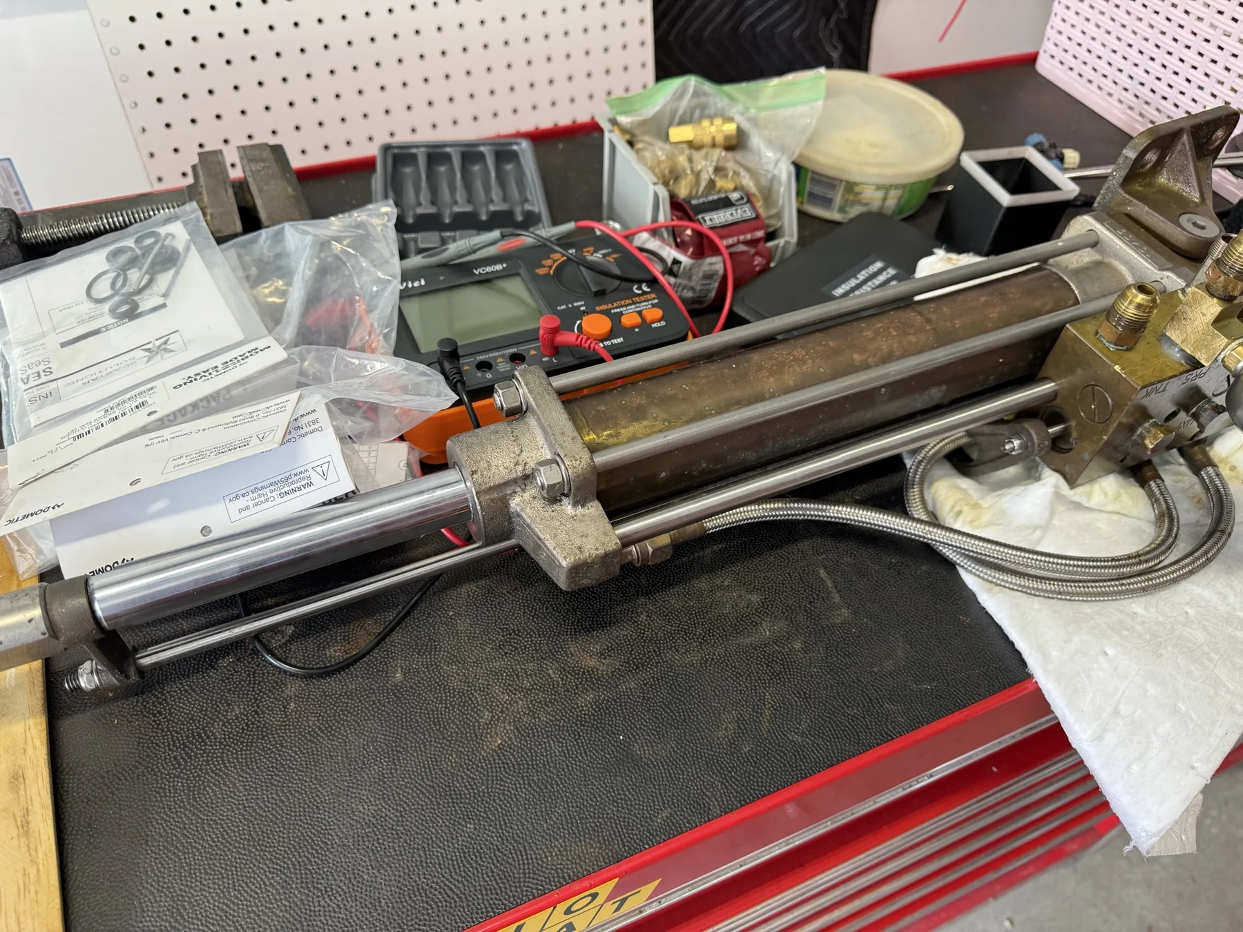 Marine steering cylinder on a workbench beside a multimeter and replacement seal kits