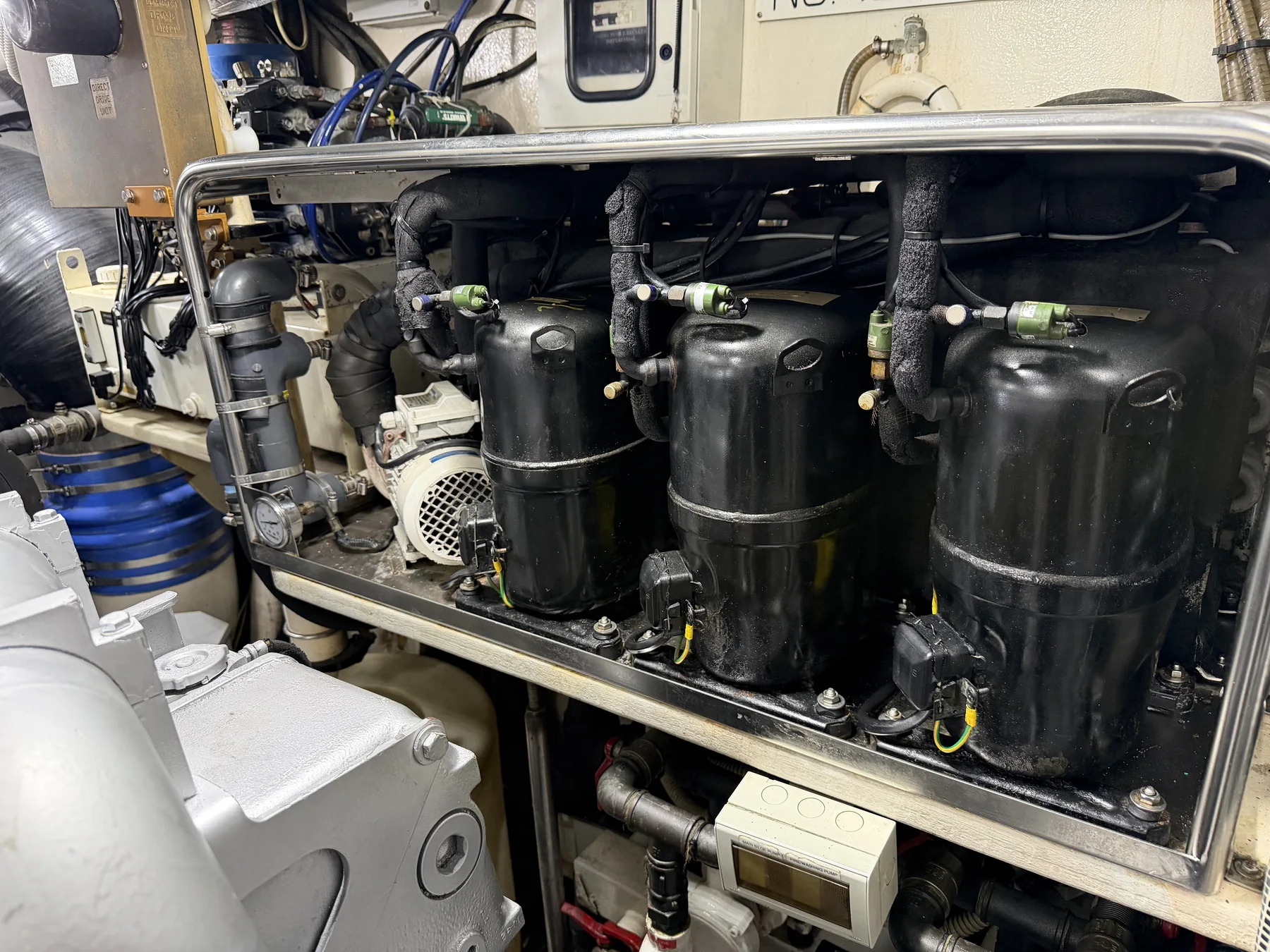 Three black refrigeration compressors and adjacent piping in a yacht engine room.