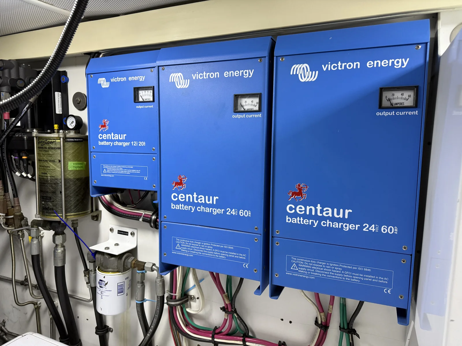 Three marine battery chargers with organized power conductors on a machinery-space bulkhead.