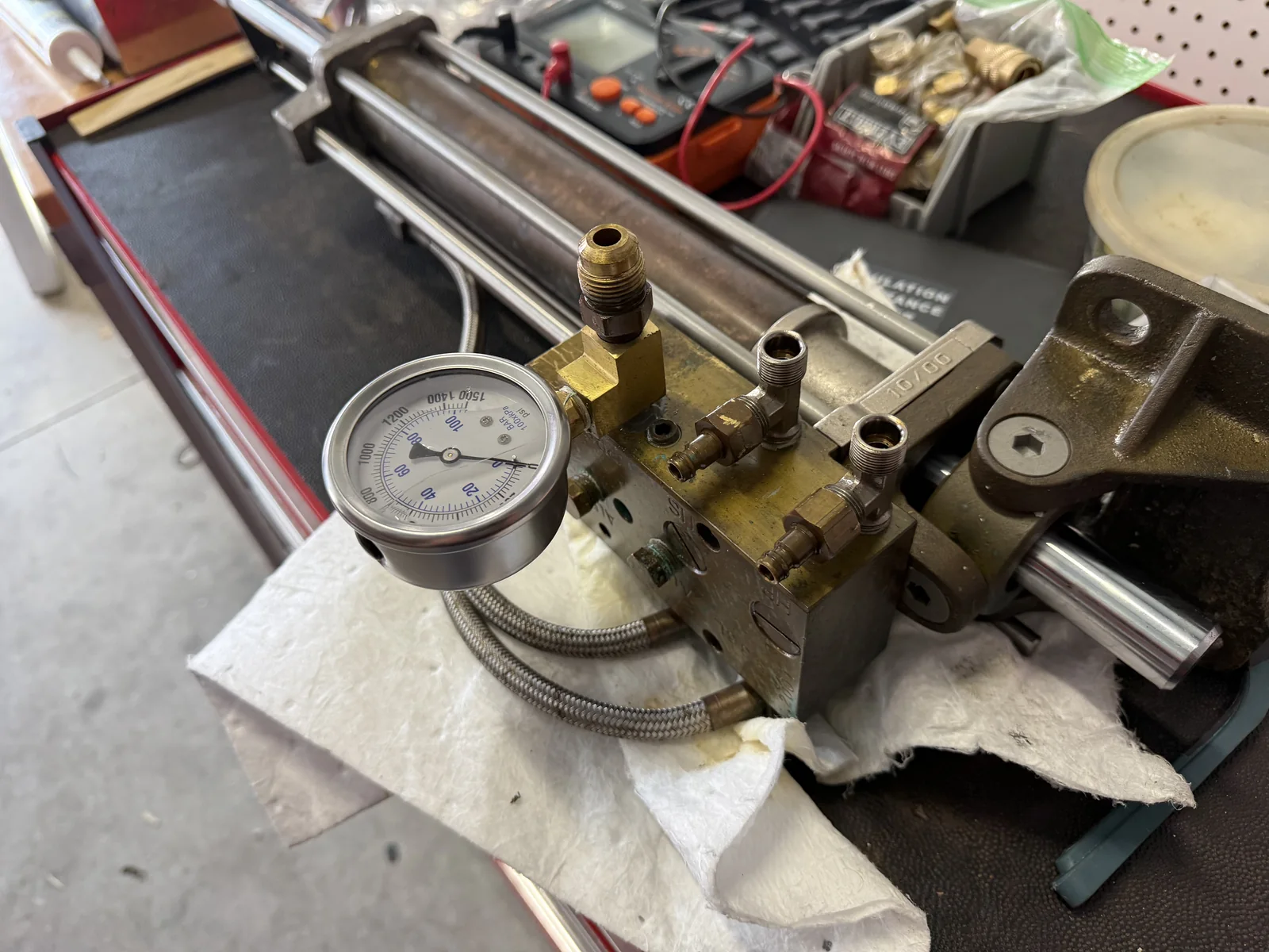 Hydraulic cylinder, manifold connections, and pressure gauge on a workbench.