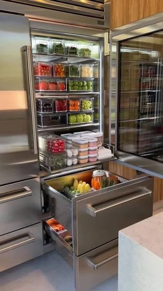 Open stainless refrigerator with organized shelves and lower freezer drawers