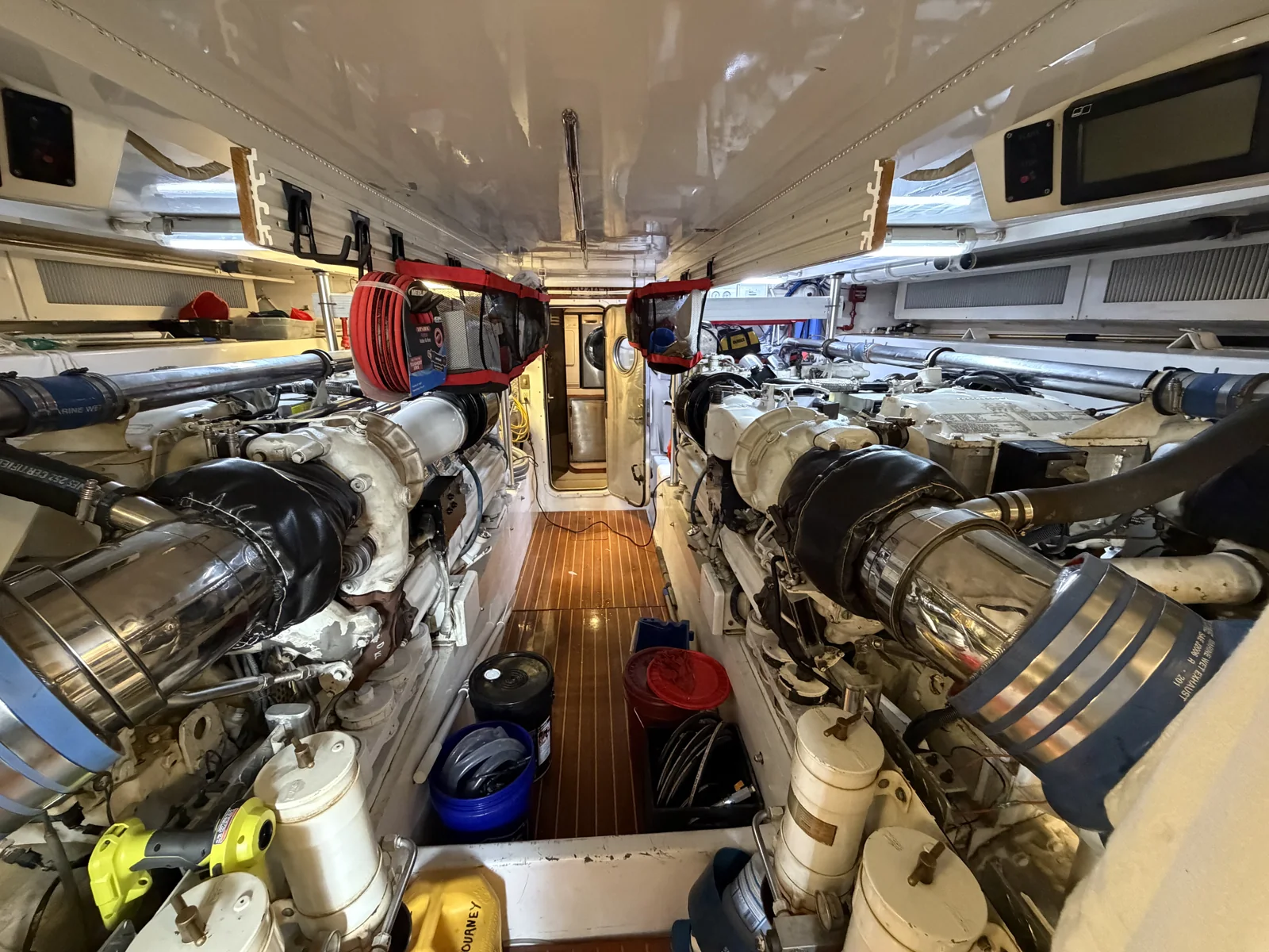 Marine engine room with twin engines, exhaust piping and an access aisle.