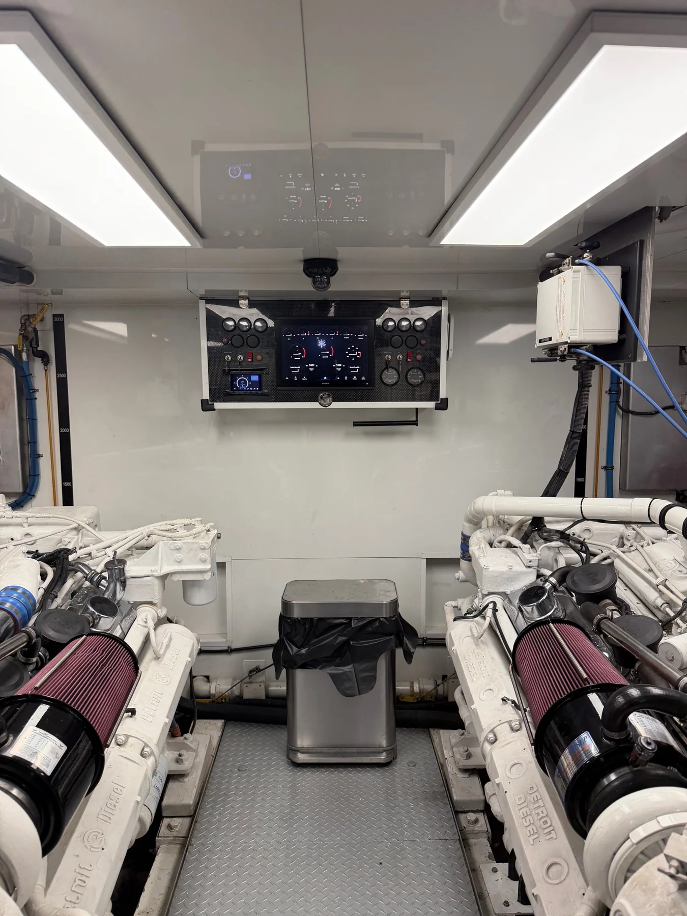 Engine room with adjacent propulsion machinery, a central control panel, and overhead lighting.